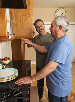 Older man pointing into open cupboard, with younger man standing by to help.